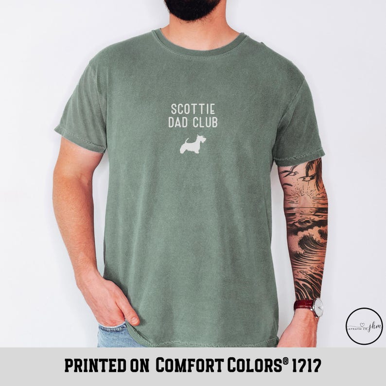 May include: Sage green t-shirt with the text "SCOTTIE DAD CLUB" and a white silhouette of a Scottish Terrier. The phrase "PRINTED ON COMFORT COLORS&reg; 1712" is printed at the bottom of the shirt.