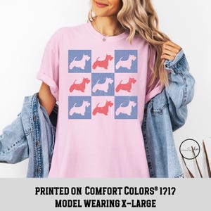 May include: Pink t-shirt with a checkered pattern of red and blue Scottish Terrier silhouettes. The text "PRINTED ON COMFORT COLORS&reg; 1212 MODEL WEARING X-LARGE" is printed below the image.