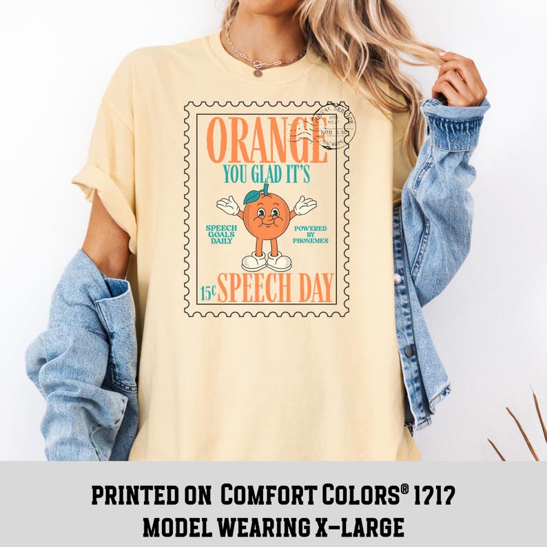 Puede incluir: Camiseta amarillo claro con un dise&ntilde;o retro de un personaje naranja, el texto "ORANGE YOU GLAD IT'S" y "15&cent; SPEECH DAY". La camiseta est&aacute; impresa en Comfort Colors 1212. La modelo lleva una talla X-Large.