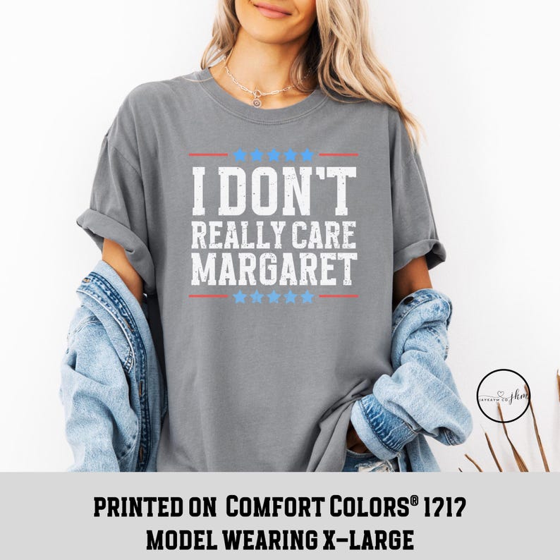 May include: Gray t-shirt with the text "I DON'T REALLY CARE MARGARET" printed in white with red stars above and below the text. The model is wearing a size X-Large.