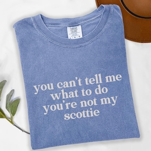 Puede incluir: Una camiseta azul Comfort Colors con el texto "you can't tell me what to do you're not my scottie" en blanco. La camiseta est&aacute; doblada y tiene cuello redondo.