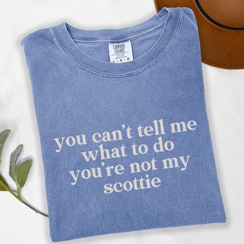 Puede incluir: Una camiseta azul Comfort Colors con el texto "you can't tell me what to do you're not my scottie" en blanco. La camiseta est&aacute; doblada y tiene cuello redondo.