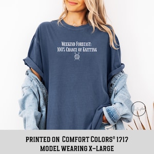 May include: A navy blue t-shirt with the text "WEEKEND FORECAST: 100% CHANCE OF KNITTING" and a small graphic of yarn and knitting needles. The model is wearing a size X-Large.