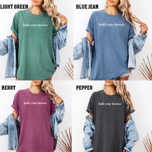 Op de afbeelding: Vier verschillende gekleurde T-shirts met de tekst "hold your horses" bedrukt op de voorkant. De T-shirts zijn lichtgroen, blauw, bordeauxrood en antraciet.