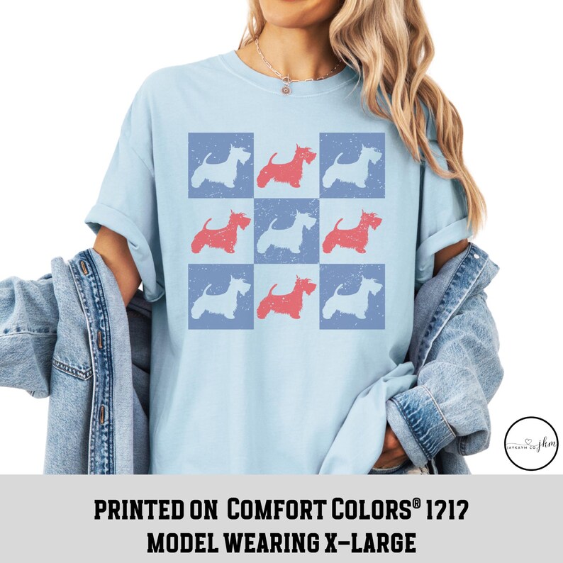 May include: A light blue t-shirt with a pattern of red and blue Scottish Terrier silhouettes. The text "PRINTED ON COMFORT COLORS&reg; 1212 MODEL WEARING X-LARGE" is printed below the image.
