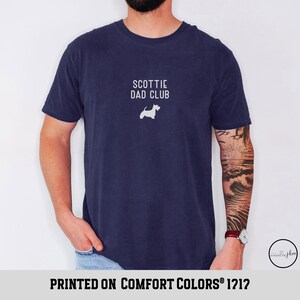 May include: Navy blue t-shirt with the text "SCOTTIE DAD CLUB" and a white silhouette of a Scottish Terrier. The shirt is printed on Comfort Colors 1212.
