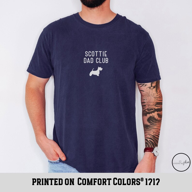 May include: Navy blue t-shirt with the text "SCOTTIE DAD CLUB" and a white silhouette of a Scottish Terrier. The shirt is printed on Comfort Colors 1212.