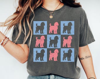 May include: Dark gray t-shirt featuring a grid pattern of dog silhouettes in black and pink, set against blue squares. The design has a distressed, vintage look. The shirt is a casual wear item.