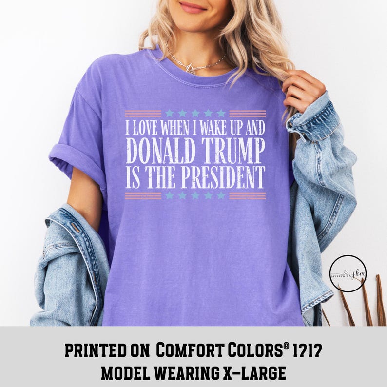 Op de afbeelding: Paars T-shirt met de tekst "I love when I wake up and Donald Trump is the President" erop gedrukt. De tekst is wit met rode en blauwe sterren erboven en eronder. Het shirt is gedrukt op Comfort Colors&reg; 1212 en het model draagt maat XL.