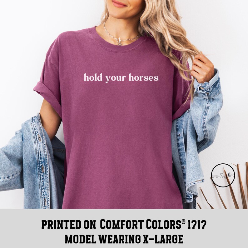 Op de afbeelding: Een mauve t-shirt met de tekst "hold your horses" in wit gedrukt op de voorkant. Het model draagt maat XL.