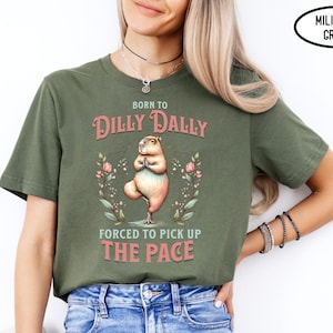 May include: A green t-shirt with the text "Born to Dilly Dally, Forced to Pick Up The Pace" in pink. A cartoon capybara is doing yoga in the centre of the shirt.