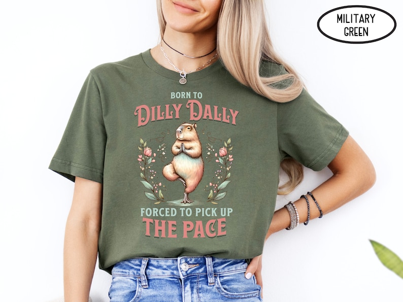May include: A green t-shirt with the text "Born to Dilly Dally, Forced to Pick Up The Pace" in pink. A cartoon capybara is doing yoga in the centre of the shirt.