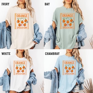 Pu&ograve; includere: Quattro magliette a maniche corte nei colori avorio, bay, bianco e chambray. Ogni maglietta presenta una stampa grafica di arance cartoon con il testo ORANGE you glad it's SPEECH DAY. Una giacca di jeans blu &egrave; appoggiata sulle spalle di ogni maglietta.