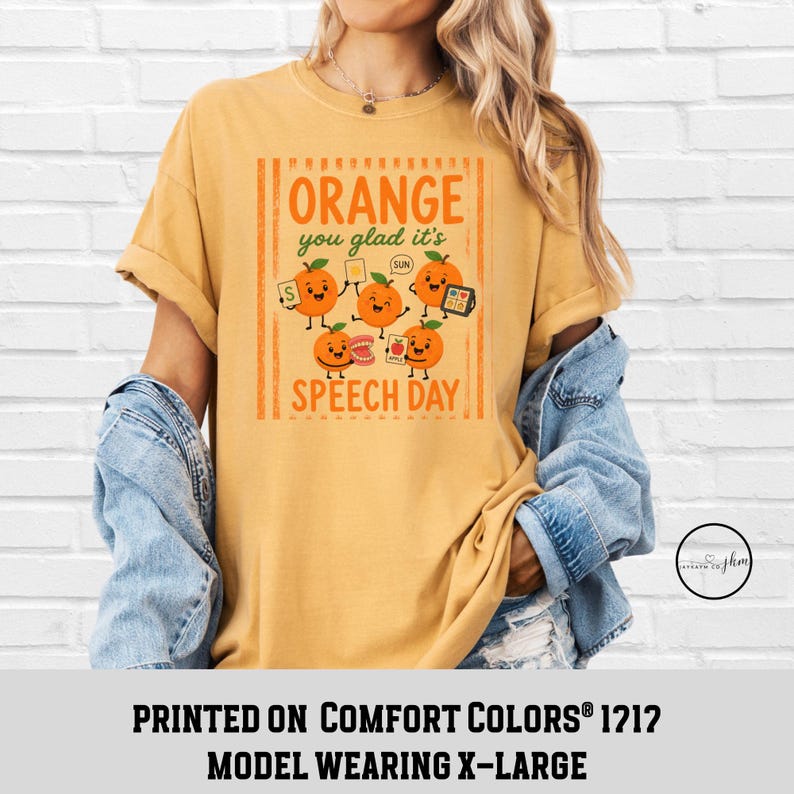 Pu&ograve; includere: Una t-shirt giallo senape con una grafica di cinque arance cartoon con braccia e gambe. Il testo recita "ORANGE you glad it's SPEECH DAY" con illustrazioni di strumenti di logopedia come flashcard e un modello di denti.