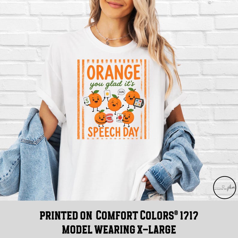 Pu&ograve; includere: Una t-shirt bianca con una grafica di cinque arance cartoon con volti e arti. Il testo recita Orange you glad it's SPEECH DAY. Le arance tengono in mano strumenti di logopedia come flashcard, un tablet e modelli di denti.