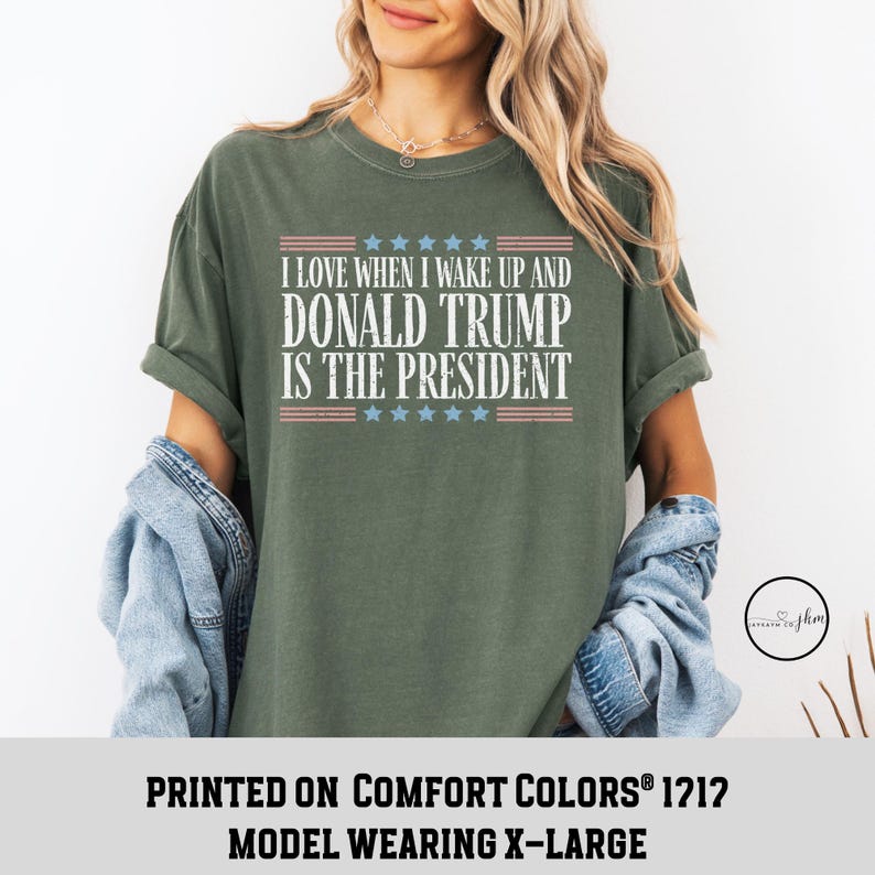 Op de afbeelding: Groen T-shirt met een witte afbeelding waarop staat "Ik hou ervan om wakker te worden en Donald Trump is president". De afbeelding bevat ook een rood-wit-blauw Amerikaans vlagontwerp. Het shirt is gedrukt op Comfort Colors&reg; 1212 en het model draagt maat XL.