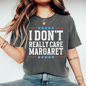 May include: A dark grey t-shirt with a distressed white graphic that reads "I don't really care Margaret" with red and blue stars above and below the text.