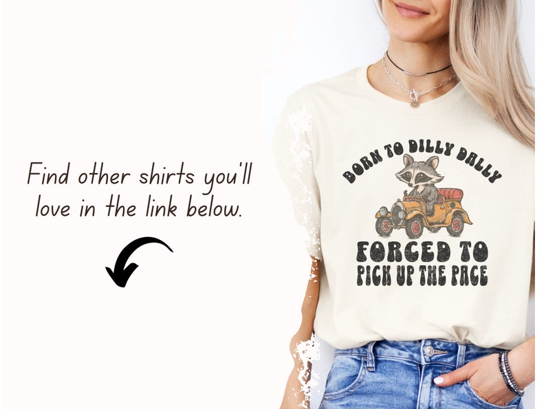 May include: A cream coloured t-shirt with a vintage graphic of a raccoon driving a car. The text on the shirt reads "Born to dilly dally, forced to pick up the pace".