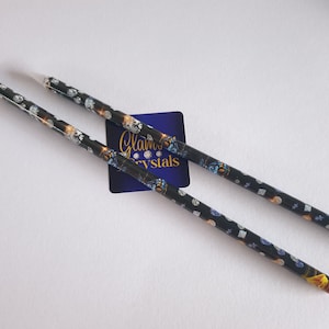 May include: Two black pencils with a white tip. The pencils are covered in a pattern of white, blue, and gold diamonds. The text "Glam Crystals" is visible on a blue square sticker.