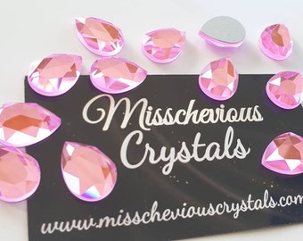 May include: Pink pear-shaped crystals with a high-shine finish. The crystals are scattered on a black surface with the text "Missschevious Crystals" and "www.missscheviouscrystals.com.au".