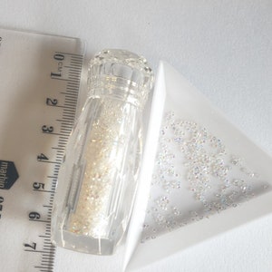 May include: A clear glass bottle filled with iridescent white glitter, next to a white triangular dish with a scattering of iridescent white glitter.