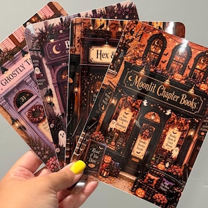 May include: A set of four rectangular prints featuring detailed illustrations of storefronts with Halloween themes. The signs read Ghostly Tales, Hex & Books, and Moonlit Chapter Books, decorated with pumpkins, ghosts, and warm lighting.