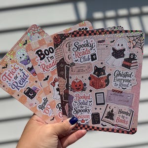 May include: A set of four rectangular holographic stickers featuring Halloween-themed illustrations of ghosts, black cats, pumpkins, and books. The text includes phrases like Spooky Reads Club, Ghosted Everyone to Read, and Haunted by Books.