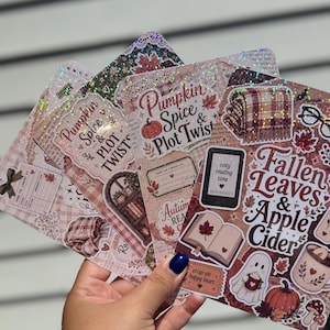 May include: A collection of rectangular stickers with a holographic finish featuring autumn-themed illustrations. Designs include text reading Pumpkin Spice & Plot Twist, Fallen Leaves & Apple Cider, cozy reading time, and crisp air happy heart.