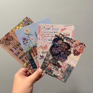 May include: A set of four rectangular bookmarks with rounded corners, featuring collage-style designs with floral motifs, butterflies, stacks of books, and inspirational text including "Accept what IS" and "find her MIND and SOUL."