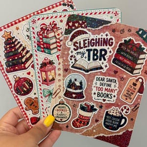 May include: Three rectangular sticker sheets featuring Christmas and book-themed illustrations. Designs include stacks of books, a snow globe, a gingerbread person, a stocking, and text reading Sleighing my TBR, Dear Santa, Define Too Many Books.