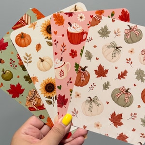 May include: A set of four rectangular cards featuring autumn-themed patterns. Designs include orange and white pumpkins with plaid bows, red mugs with whipped cream, sunflowers, red and green maple leaves, acorns, and wrapped gift boxes.
