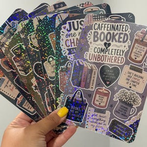 May include: A collection of rectangular holographic stickers featuring book-themed illustrations and text including CAFFEINATED BOOKED & COMPLETELY UNBOTHERED, FUELED BY ICED COFFEE, BOOKS ARE MY LOVE LANGUAGE, and various other literary-inspired graphics.