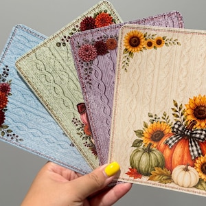 May include: Four rectangular cards with rounded corners, each featuring a textured cable knit pattern in blue, light green, purple, and cream. The cards are decorated with floral arrangements of sunflowers, pumpkins, and dahlias in autumn colors.