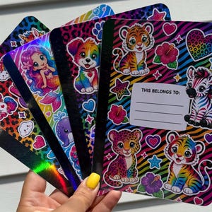 May include: A set of four composition notebooks featuring holographic covers with vibrant rainbow animal prints, including a tiger, zebra, leopard, and unicorn. Each notebook displays a white label with the printed text THIS BELONGS TO.