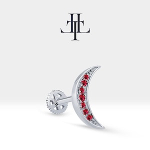 Può includere: Orecchino a forma di mezzaluna in argento con una fila di pietre preziose rosse. L'orecchino ha una chiusura a vite.