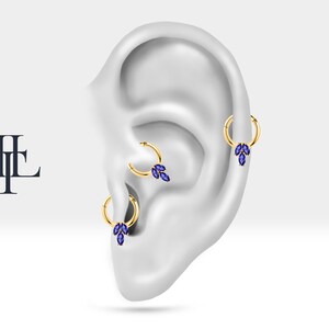May include: Three gold hoop earrings with blue marquise shaped gemstones hanging from each hoop. The earrings are displayed on a model ear.
