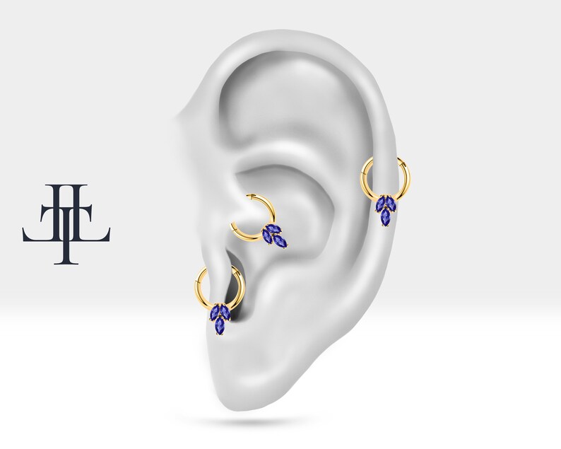 May include: Three gold hoop earrings with blue marquise shaped gemstones hanging from each hoop. The earrings are displayed on a model ear.