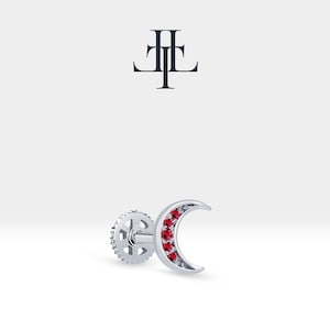 Könnte beinhalten: Silberner Halbmond-Ohrring mit roten Edelsteinen. Der Ohrring hat einen Schraubverschluss.