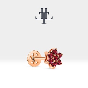 May include: A single rose gold stud earring with a flower design featuring six red gemstones.