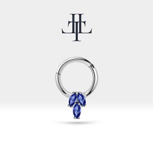 May include: A silver hoop earring with a cluster of three marquise shaped blue gemstones hanging from the bottom.