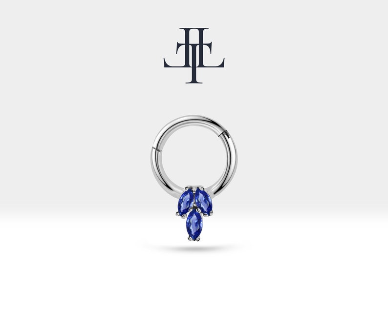 May include: A silver hoop earring with a cluster of three marquise shaped blue gemstones hanging from the bottom.