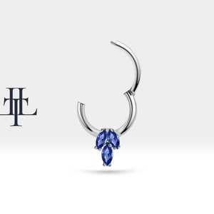 May include: A silver hoop earring with a cluster of three marquise shaped blue gemstones hanging from the bottom.