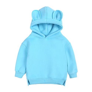 May include: A light blue hooded sweatshirt with attached bear ears on the hood. The sweatshirt has long sleeves, a kangaroo pocket, and a split hem. The garment is made of a soft, comfortable material, perfect for casual wear.