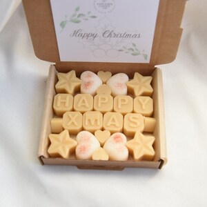 May include: A box of wax melts with a "Happy Christmas" card on top. The wax melts are shaped like stars, hearts, and letters that spell out "HAPPY XMAS".