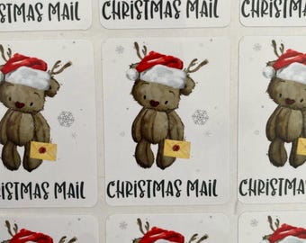 Pode incluir: Uma folha de autocolantes retangulares com um urso de peluche castanho a usar um gorro de Pai Natal vermelho e branco com hastes de rena. O urso segura um envelope amarelo com um selo de cera vermelho. O texto CHRISTMAS MAIL está impresso a preto.