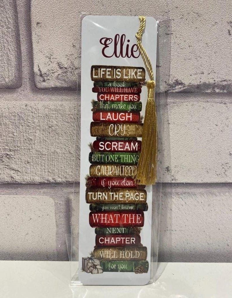 May include: A bookmark with a gold tassel, featuring a stack of books with the text "Life is like a book..." and the name "Ellie" in a decorative font. The bookmark has a white background.