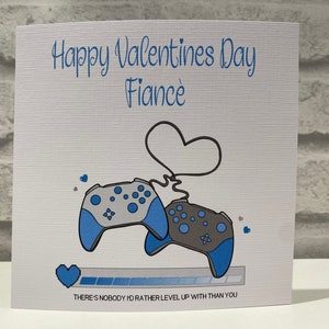 May include: A white card with blue and grey illustrations of video game controllers. The card reads "Happy Valentines Day Fiancé" and "There's nobody I'd rather level up with than you".