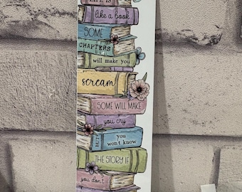 Pode incluir: Um marcador de página retangular com uma pilha de livros ilustrados coloridos e uma borboleta no topo. O texto diz: LIFE IS like a book SOME CHAPTERS will make you scream SOME WILL MAKE you cry BUT you won't know THE STORY IF you don't TURN THE page.