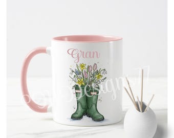 Pode incluir: Caneca de cerâmica branca com interior e alça rosa. A caneca apresenta uma ilustração em aquarela de galochas verdes cheias de flores coloridas. A palavra "Gran" está escrita em rosa.