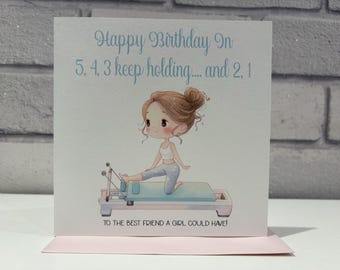 Pode incluir: Um cartão de aniversário com uma ilustração de desenho animado de uma menina em uma máquina de reformer de Pilates. O cartão tem o texto "Happy Birthday In 5, 4, 3 keep holding... and 2, 1" em azul claro. A parte inferior do cartão diz "TO THE BEST FRIEND A GIRL COULD HAVE!"